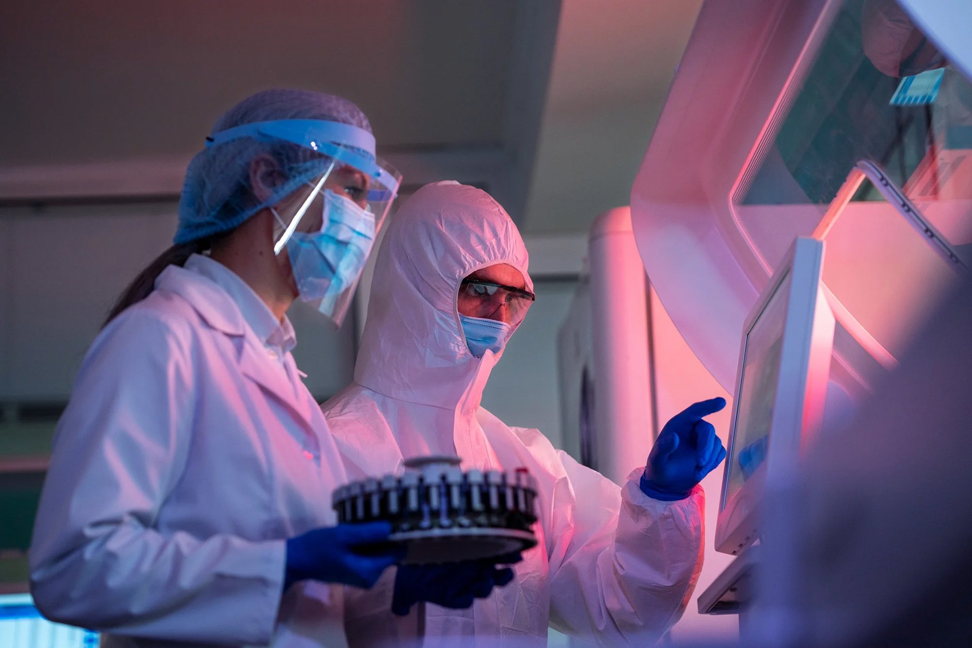 Forskere i beskyttelsesudstyr betjener en touchscreen-maskine i et laboratorium med specialudstyr.