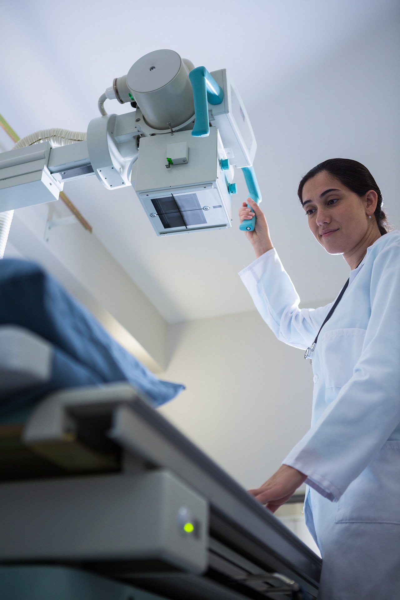 Radiologteknolog, der justerer en røntgenmaskine over et patientbord.