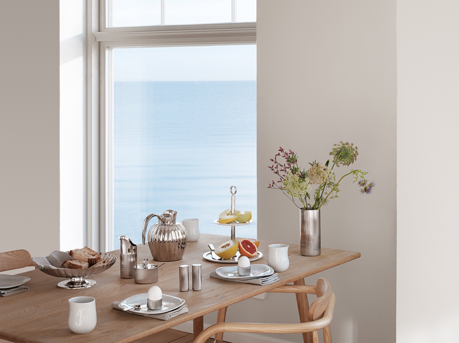 Elegant morgenbord med sølvtøj og havudsigt gennem et stort vindue.