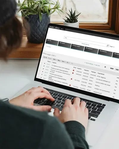 En person skriver på en bärbar dator som visar gränssnittet för Acadre från Formpipe, med uppgiftsdetaljer, deadlines och kategorier i en ljus inomhusmiljö.