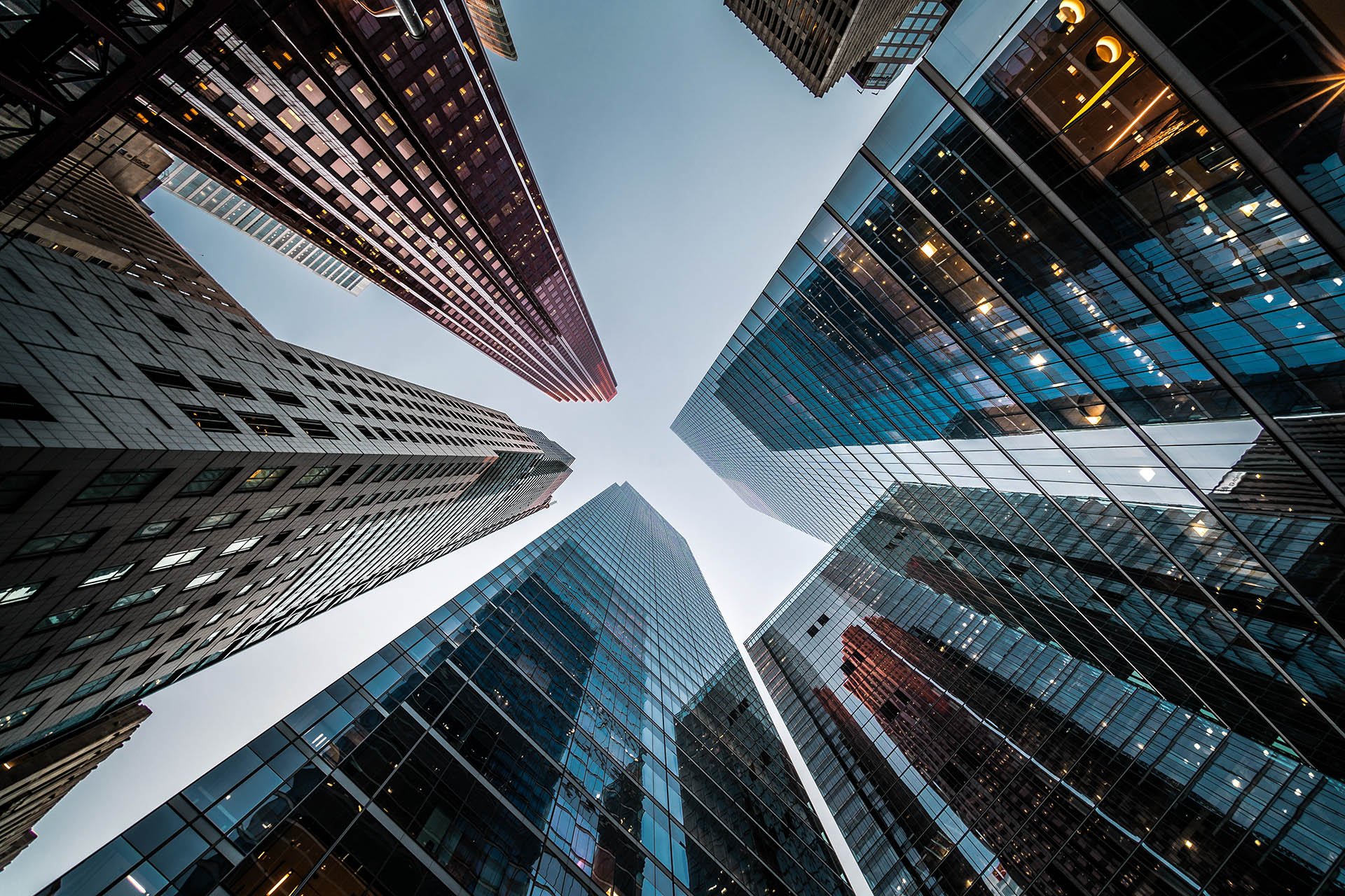 View of several modern skyscrapers shot from below, converging towards the sky, with glass and steel facades reflecting the surrounding buildings. View of several modern skyscrapers shot from below, converging towards the sky, with glass and steel facades reflecting the surrounding buildings.